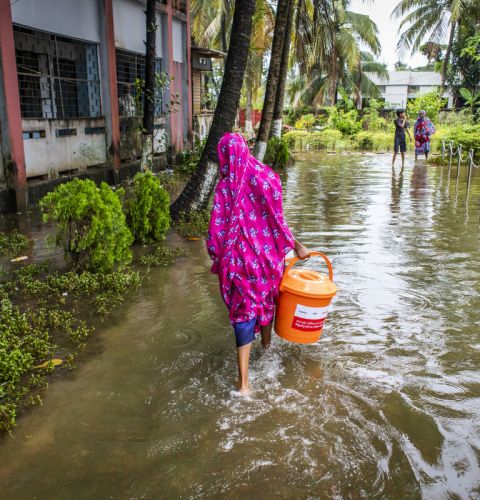 Woman wades through floods in Bangladesh carrying supplies.