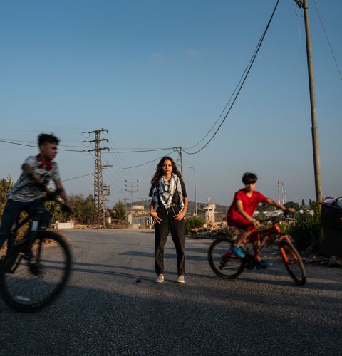 Girl standing in the road with brothers on bikes cycling around her.