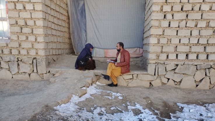 A woman sits on the ground with snow around, speaking to a man in Afghanistan